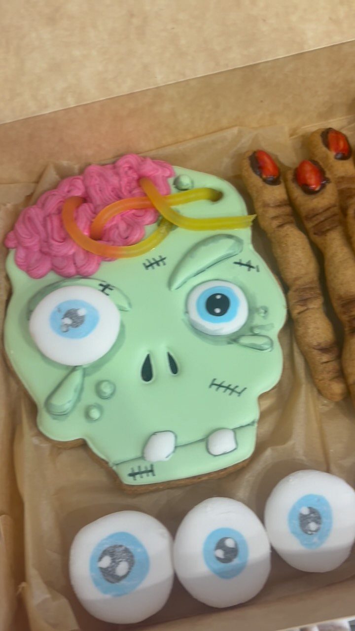Halloween decorated cookies featuring a zombie face, fingers, and eyeballs in a box.