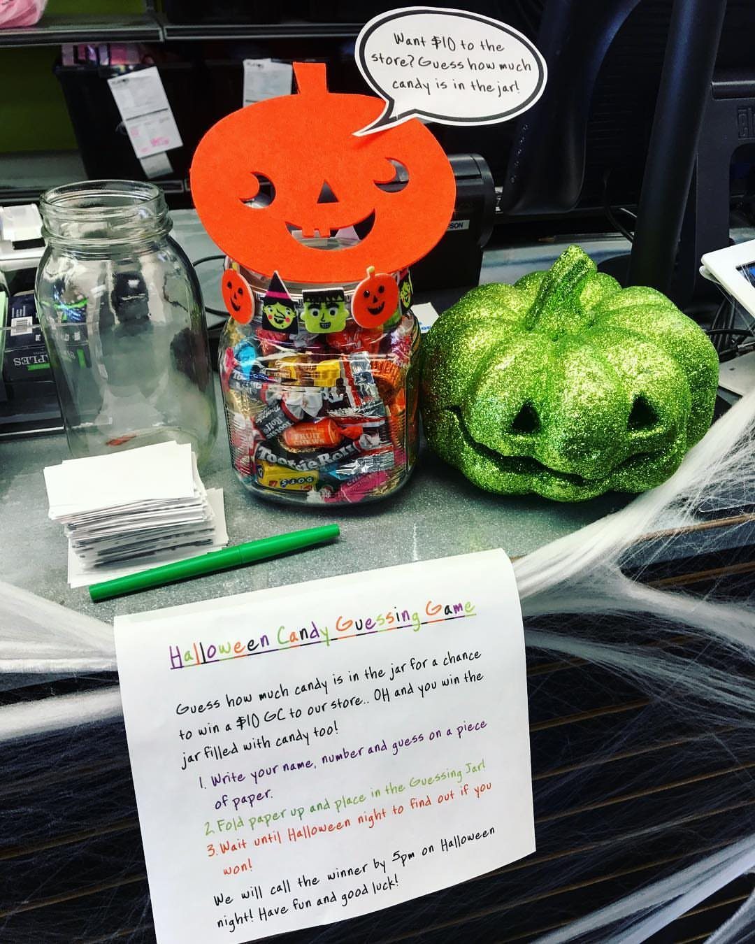 Jar of colorful candies with a pumpkin decoration and guessing game instructions.