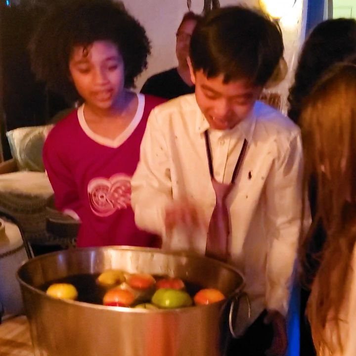 Boy leaning over a metal tub of floating apples for apple bobbing game