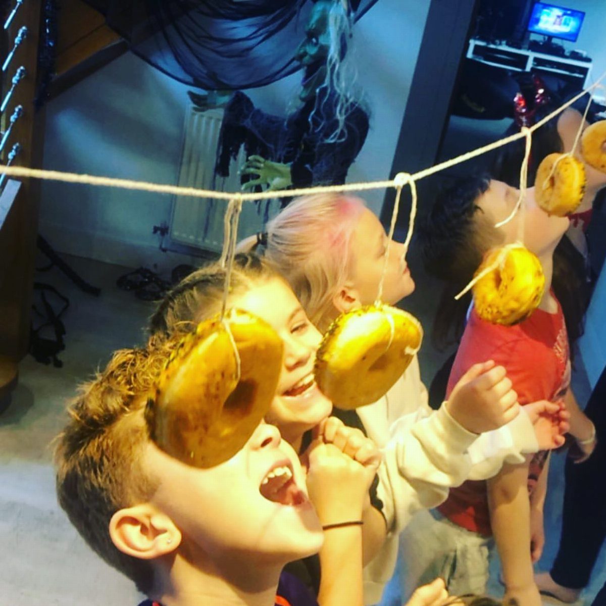 Children trying to eat glazed donuts hanging from a string at a party.