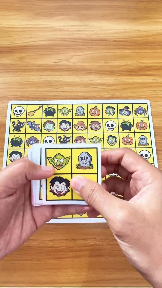 Hands holding Halloween themed memory game cards over a matching grid board.