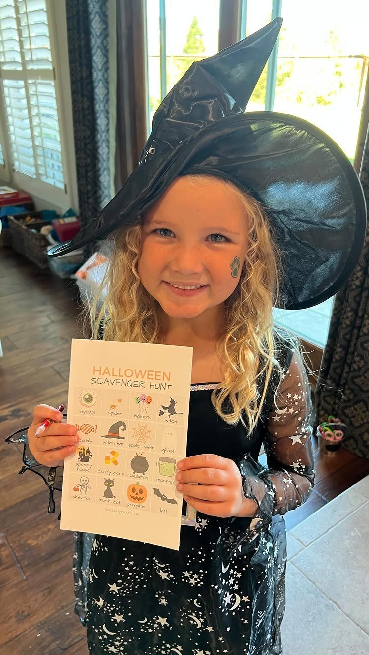 Girl in witch costume holding a Halloween scavenger hunt checklist with illustrated icons.