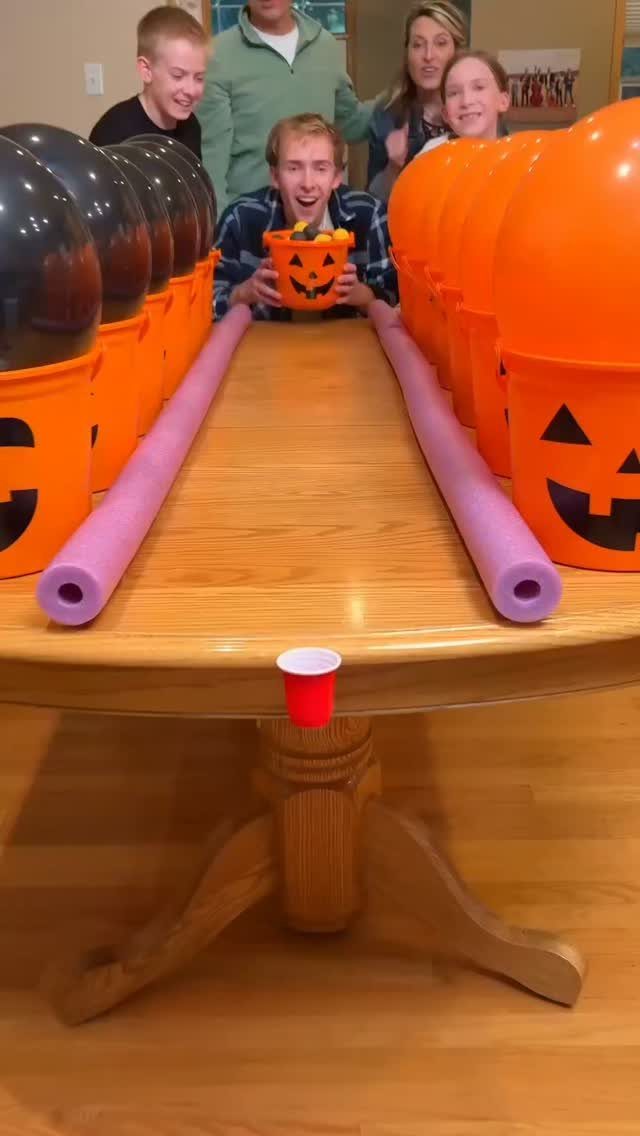Children playing a Halloween balloon game with pumpkin buckets on a wooden table