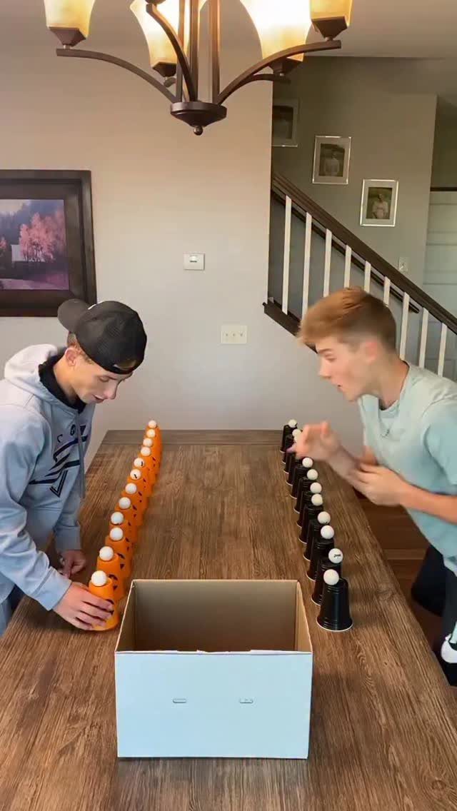 Two young men playing a bowling game with orange and black pins on a table