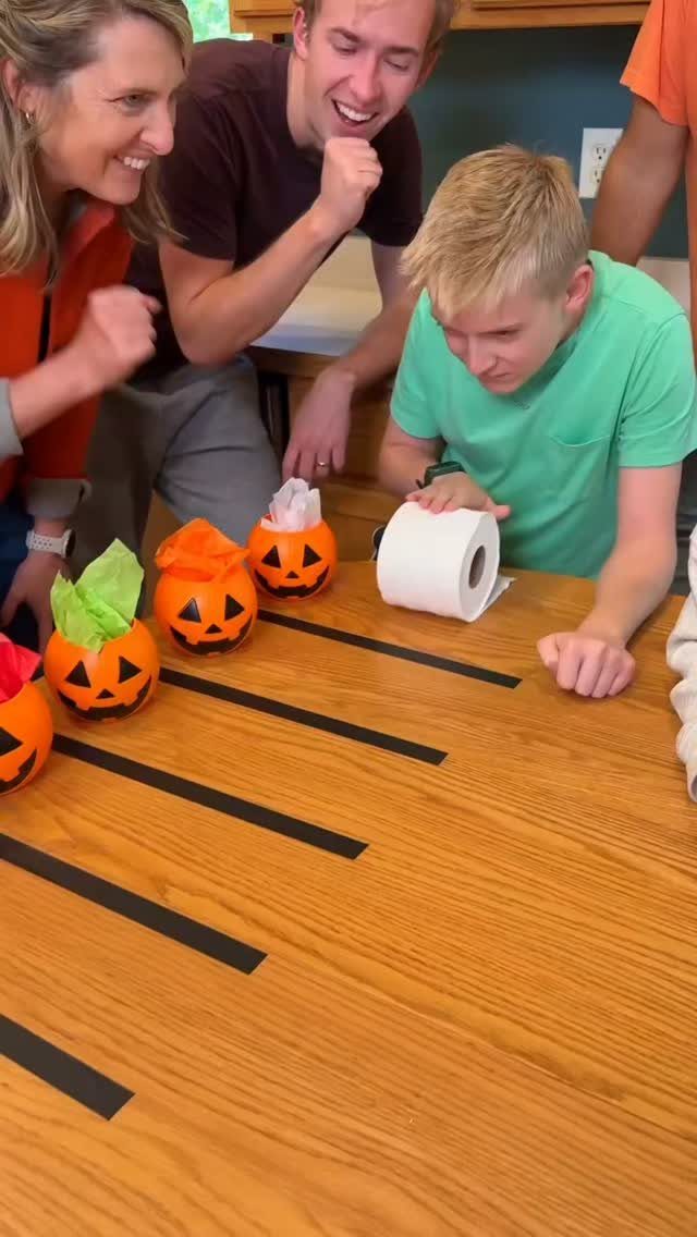 Boy rolling toilet paper toward pumpkin buckets during a Halloween game for kids