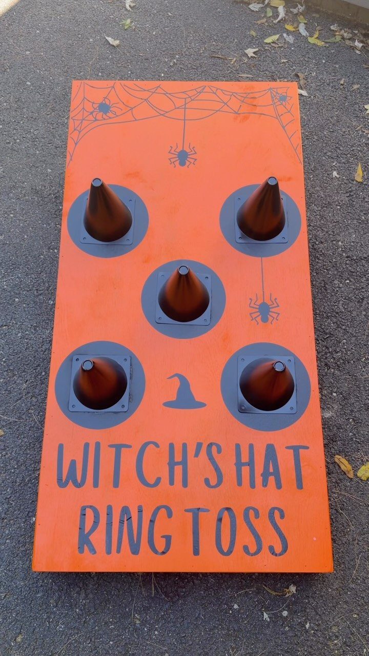 Orange wooden game board with five brown witch hats for a ring toss game.