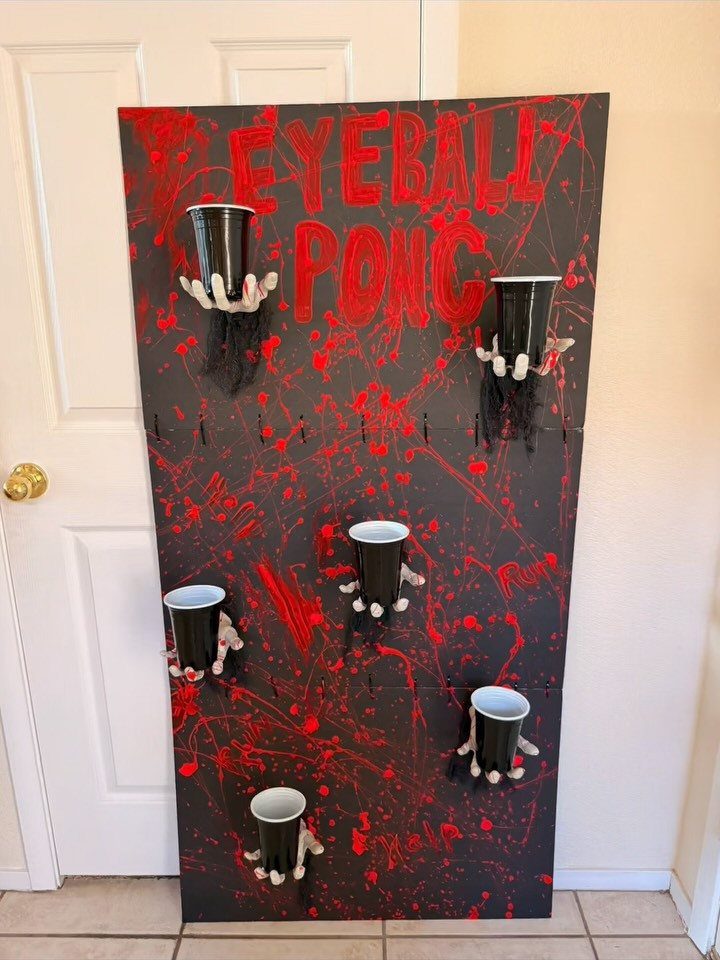 Eyeball Pong game board with black cups held by zombie hands on red splattered background
