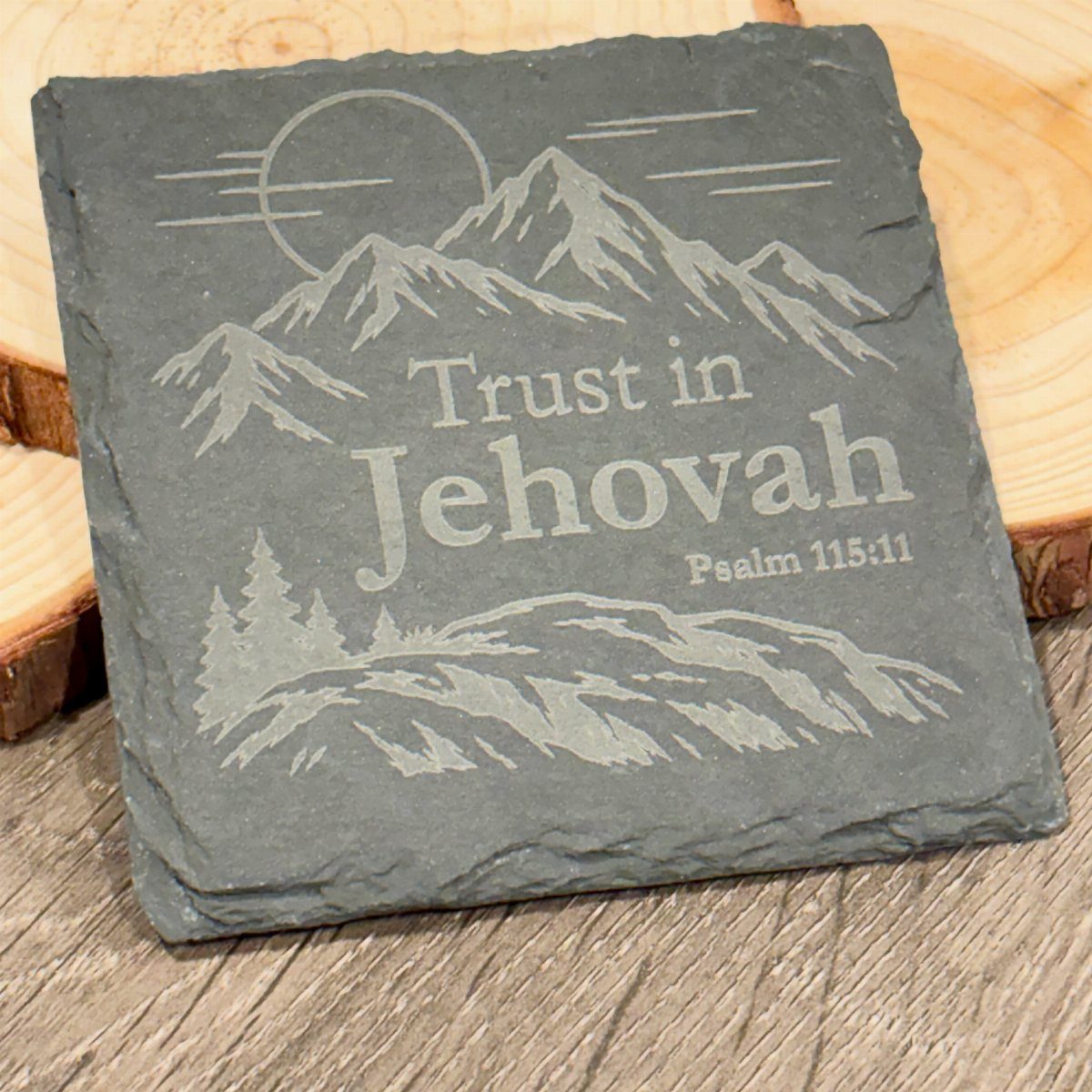 Engraved slate coaster featuring mountains and a biblical quote on a wooden surface