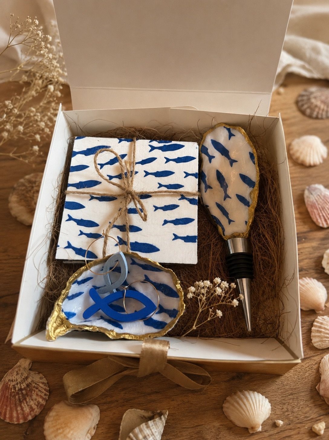 Gift box with fish-themed resin accessories, napkins, and seashells on wooden background