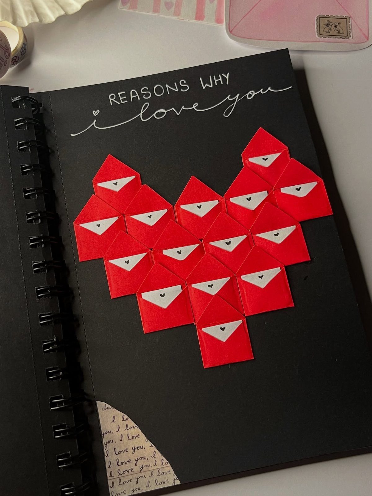 Black notebook page with red envelopes arranged in a heart shape and handwritten text.