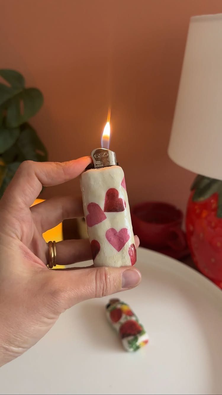 Hand holding a lit lighter with a white clay cover decorated with hearts.