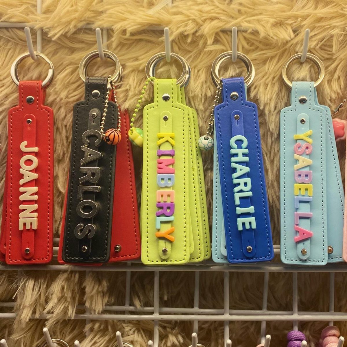 Personalized leather keychains in various colors hanging on a white metal display rack.