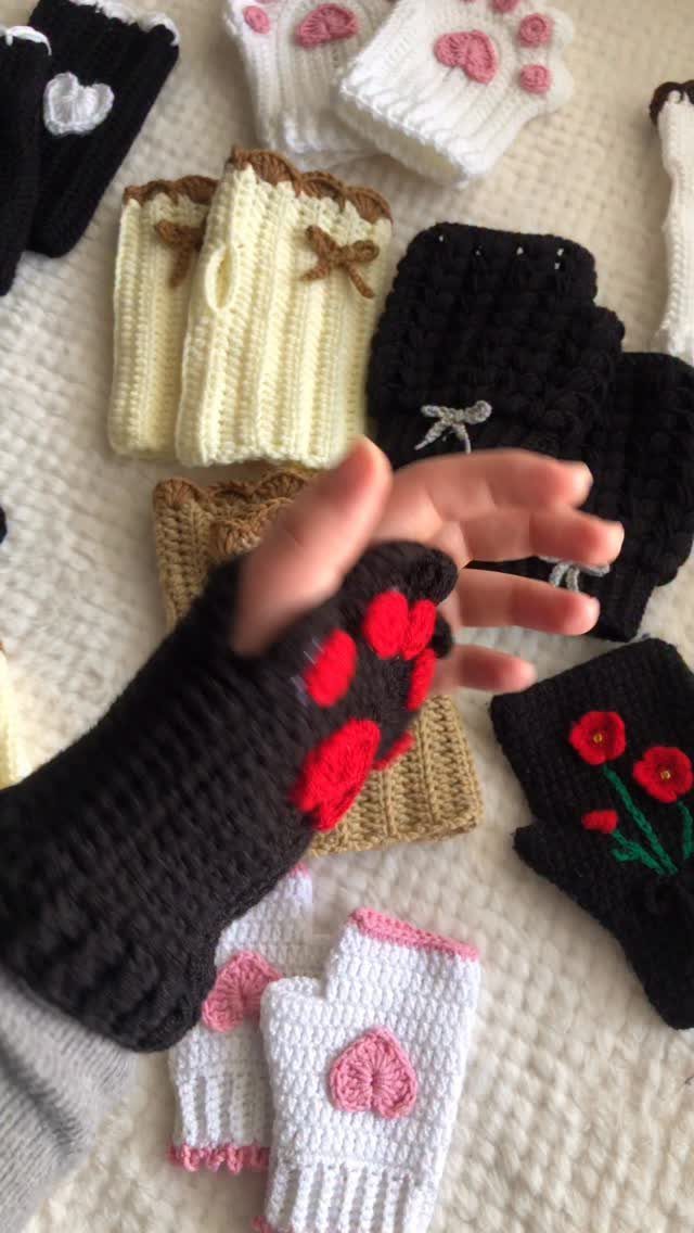 Handmade knitted fingerless gloves with paw prints and hearts on white fabric.