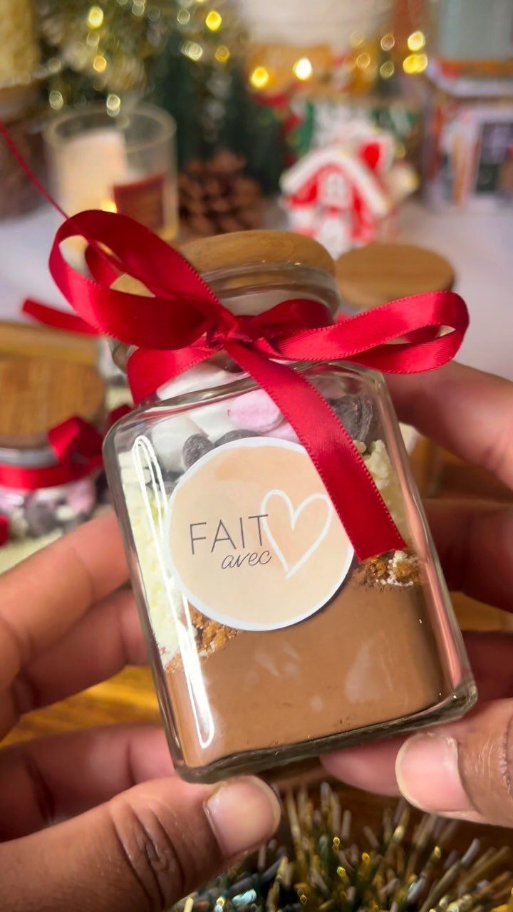 Glass jar filled with layered hot cocoa mix tied with a red ribbon.