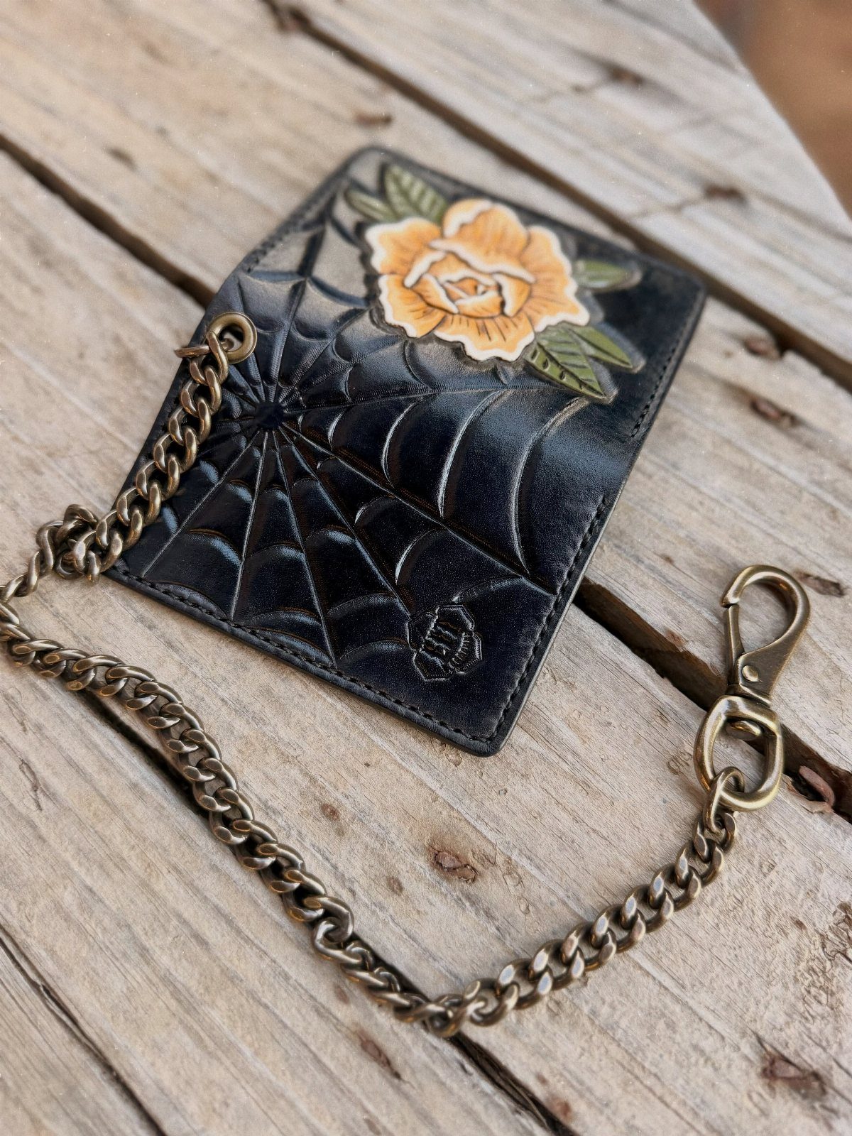 Black leather wallet with spiderweb embossing and yellow rose on wooden planks
