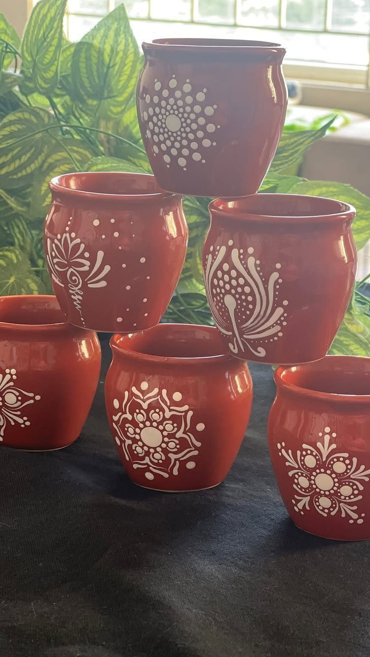 Reddish-brown ceramic mugs with white hand-painted floral patterns arranged on a black surface.