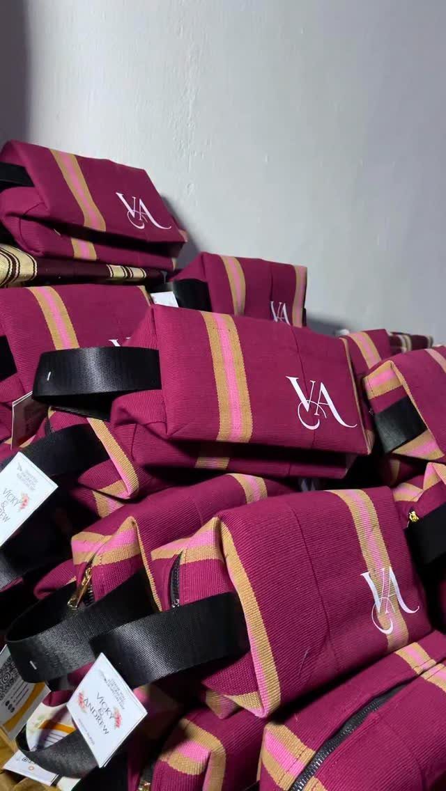 Magenta and gold striped fabric pouches with embroidered initials and black handles.