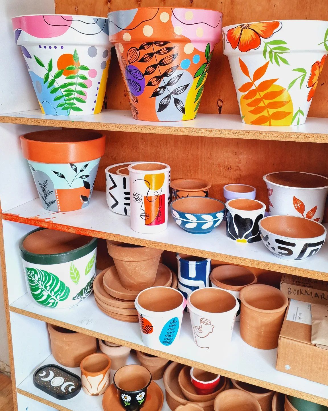 Hand-painted terracotta pots with colorful abstract designs displayed on wooden shelves