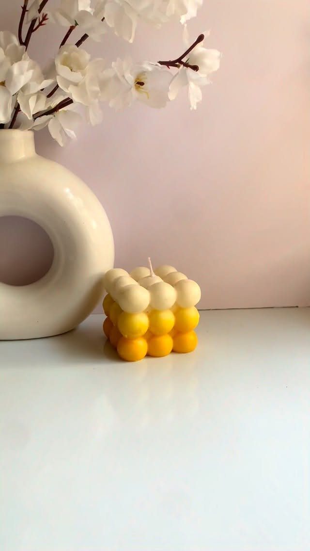 Yellow and white bubble candle next to a white vase with flowers.