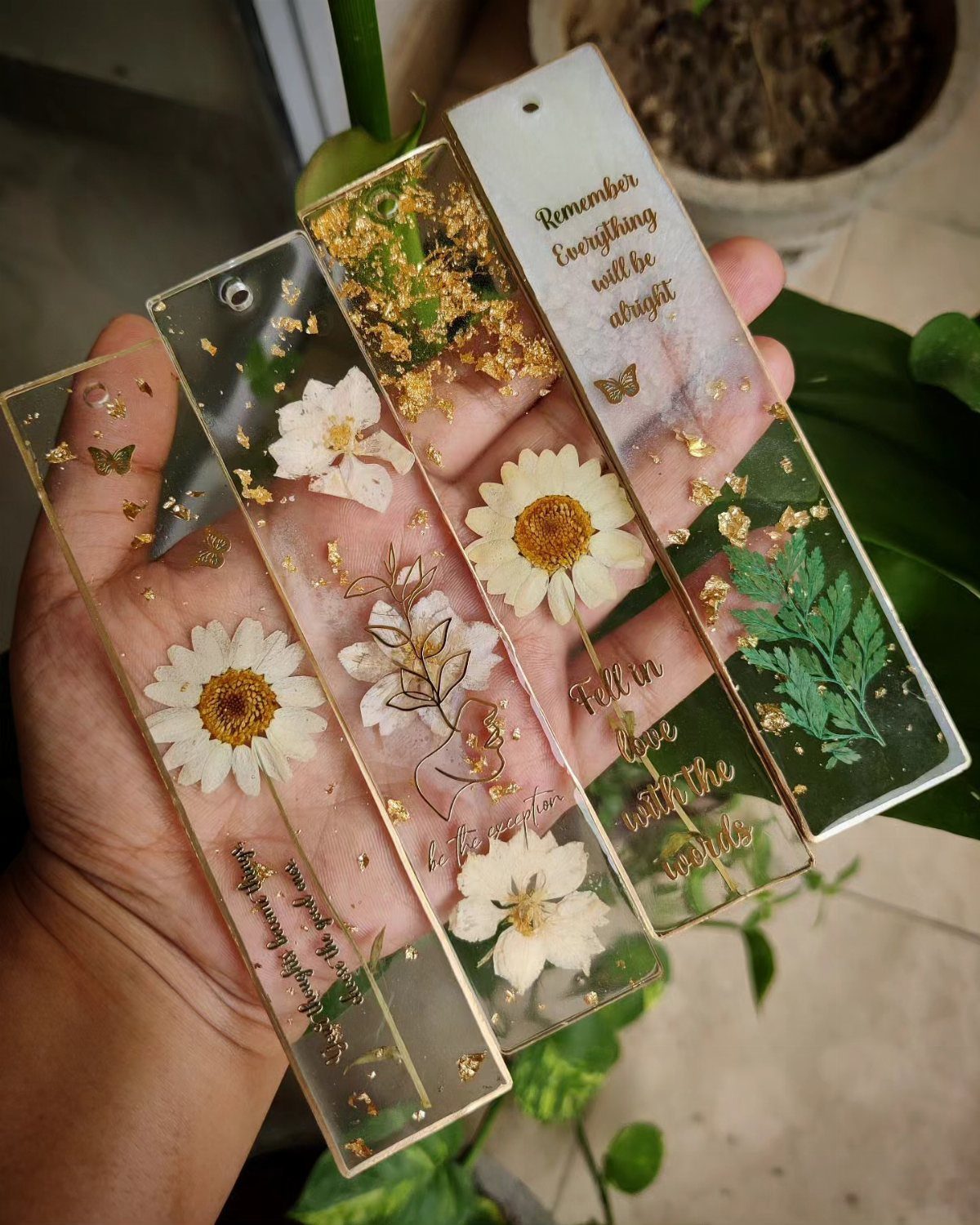 Clear resin bookmarks with pressed flowers and gold flakes held in a hand