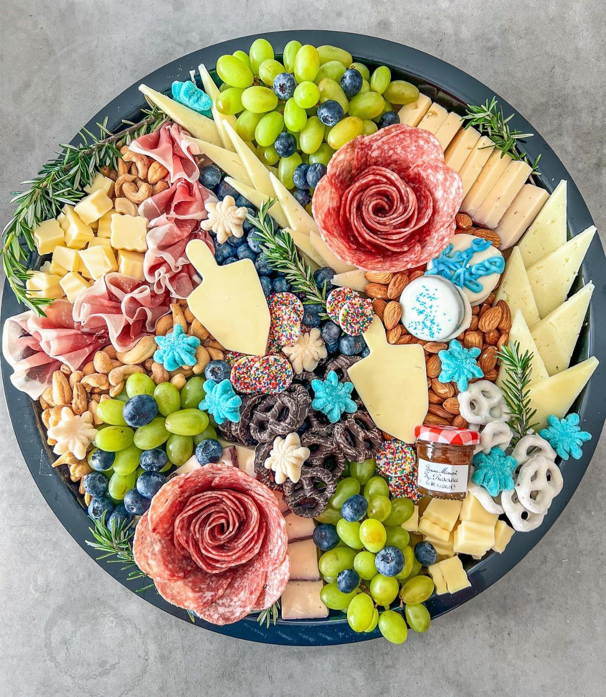 Hanukkah charcuterie board with meat roses, cheeses, fruits, and blue snowflake cookies.