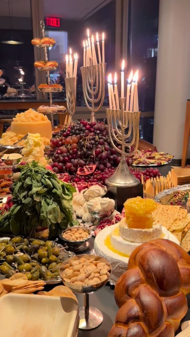 Hanukkah charcuterie spread with challah bread, cheeses, fruits, and two lit silver menorahs.