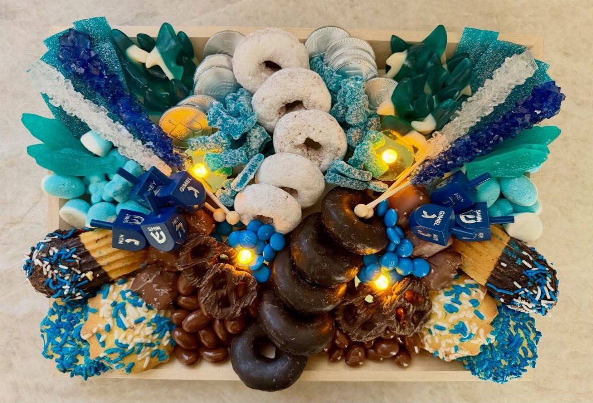 Blue and white dessert board with donuts, rock candy, and blue dreidels.