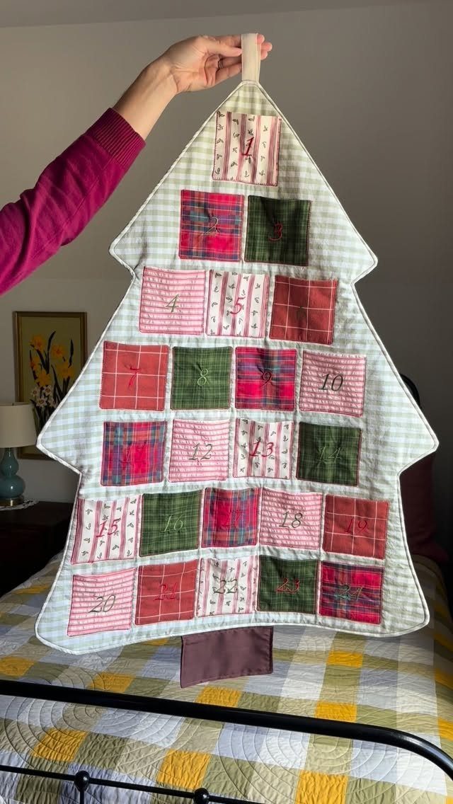 Tree-shaped fabric advent calendar with numbered red and green plaid pockets held by hand.