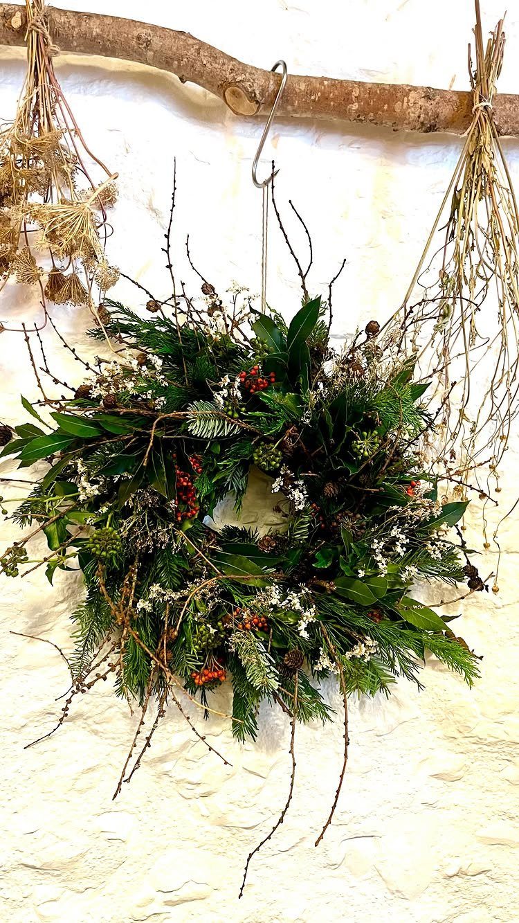 Christmas wreath with green foliage and red berries hanging on a white wall
