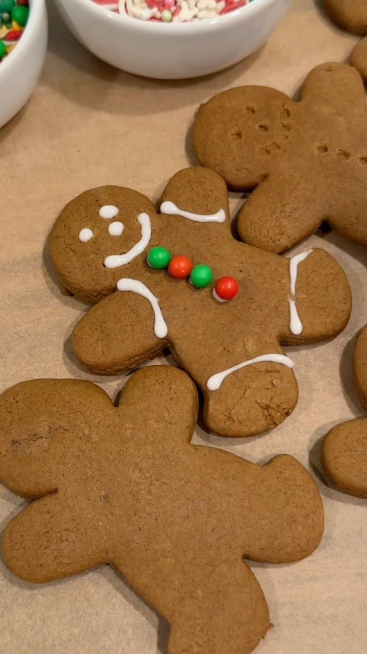 Gingerbread man cookies on parchment paper, one decorated with icing and colorful candies.