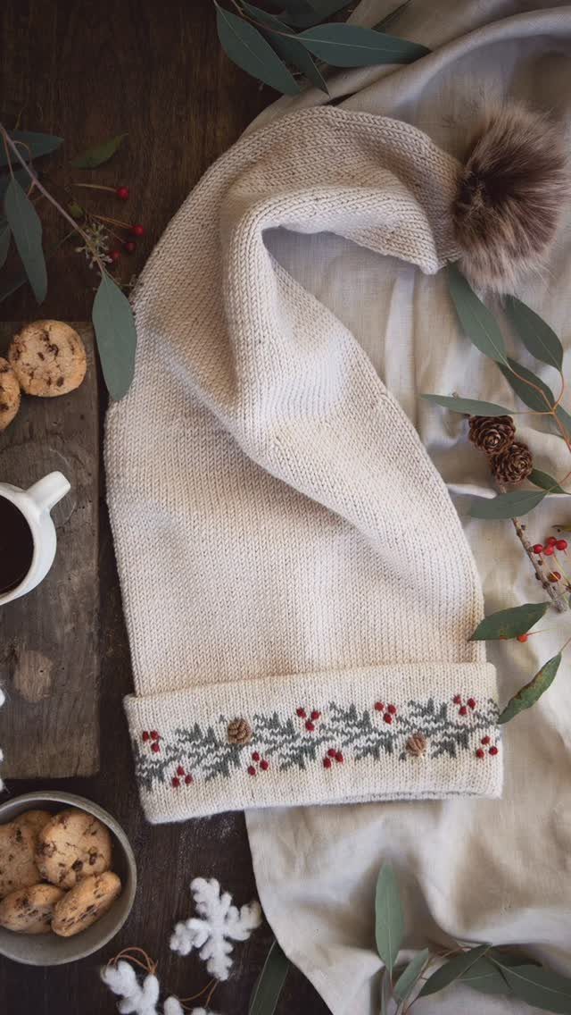 Cream knitted beanie hat with a fur pom-pom and festive floral border pattern.