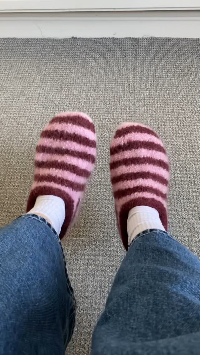 Pink and burgundy striped knitted slippers worn with white socks and blue jeans.