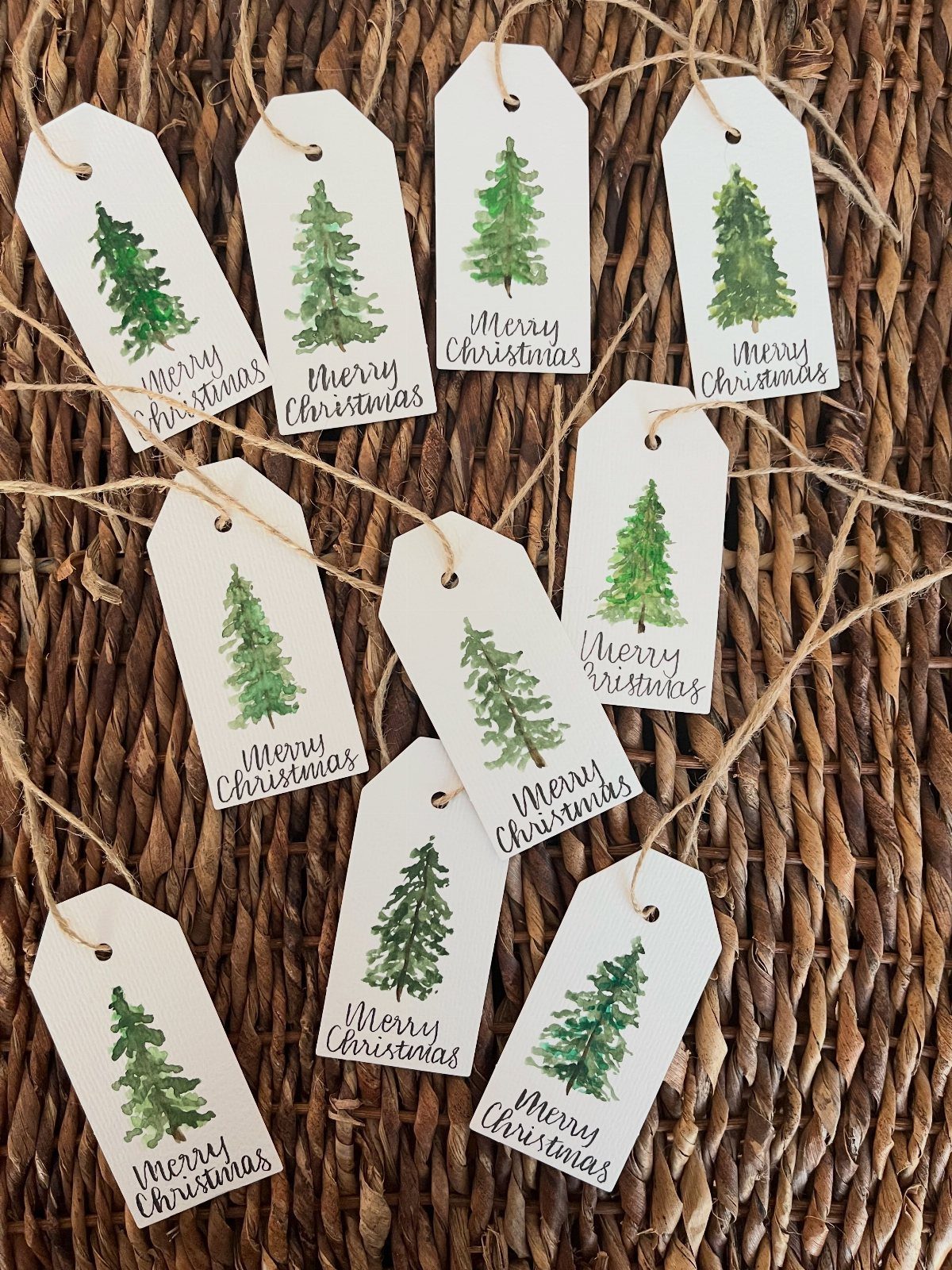 White Christmas gift tags with green trees and twine on a wicker background.