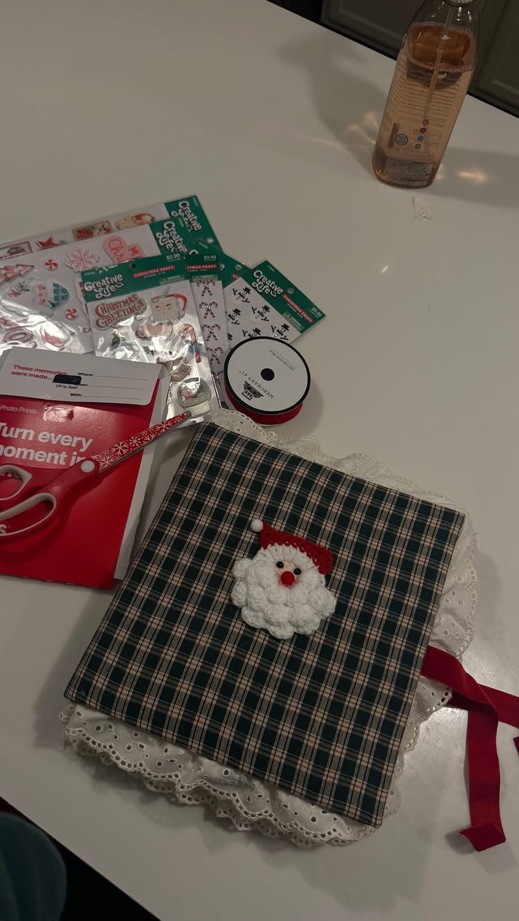 Handmade plaid fabric book with a crocheted Santa face and craft supplies.