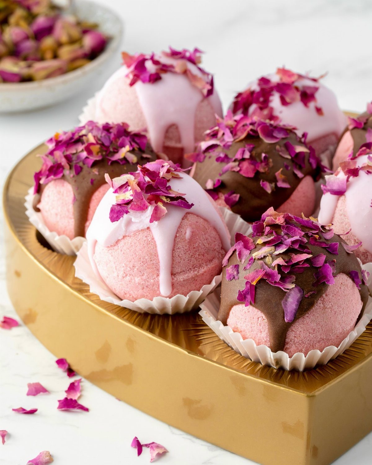 Pink bath bombs with chocolate drizzles and rose petals on a gold tray
