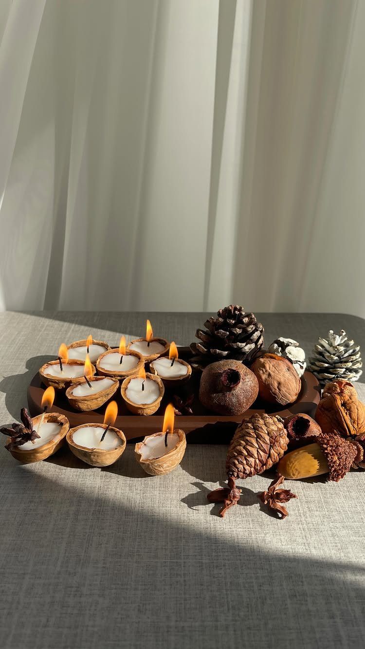 Lit candles in acorn shells on a wooden tray with pinecones and seed pods.