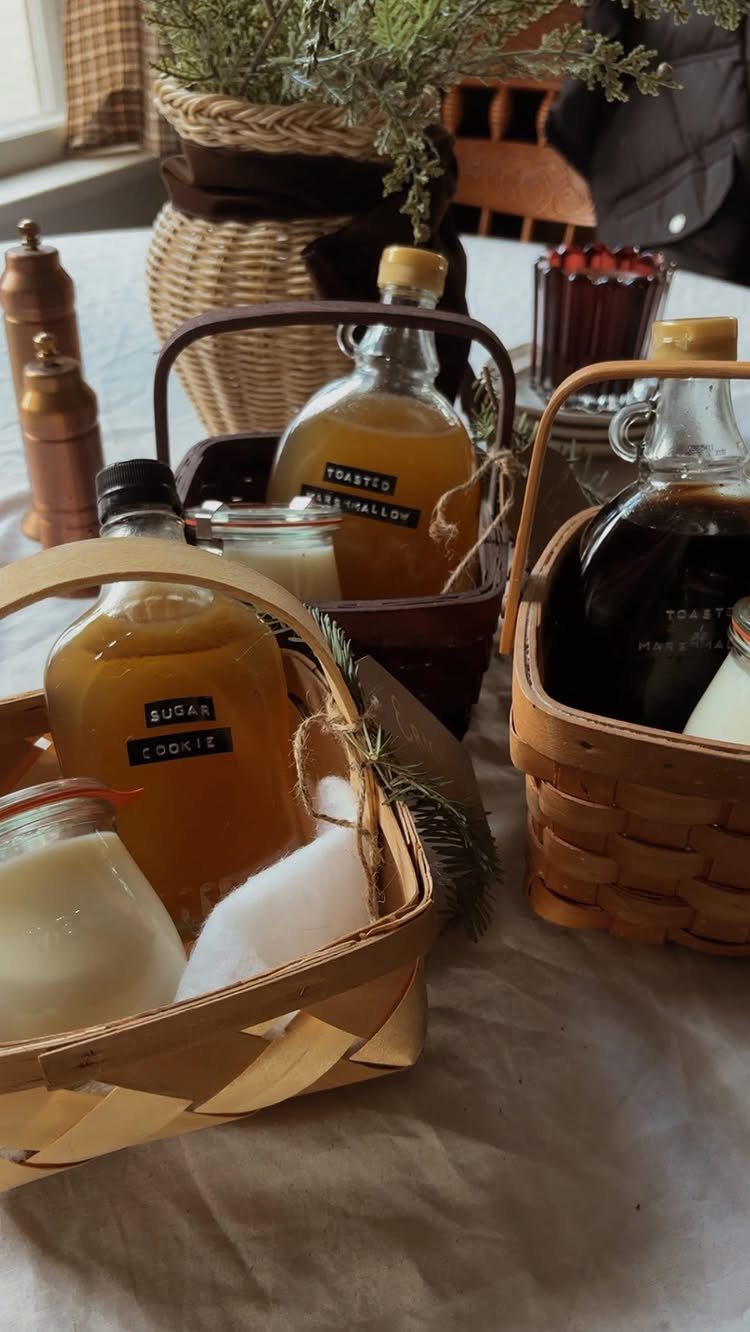 Woven gift baskets containing flavored syrup bottles and small jars on a tablecloth.