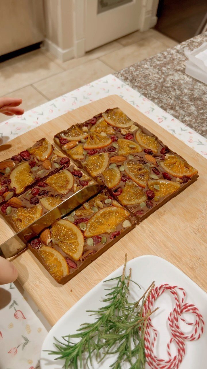 Chocolate bark with dried orange slices and nuts on a wooden cutting board.
