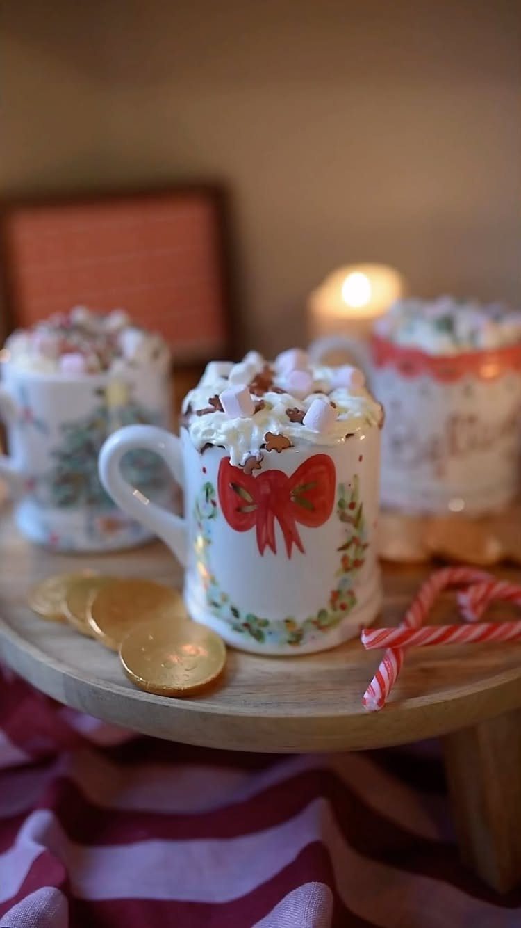 Hot chocolate mugs topped with whipped cream and marshmallows on a wooden tray.