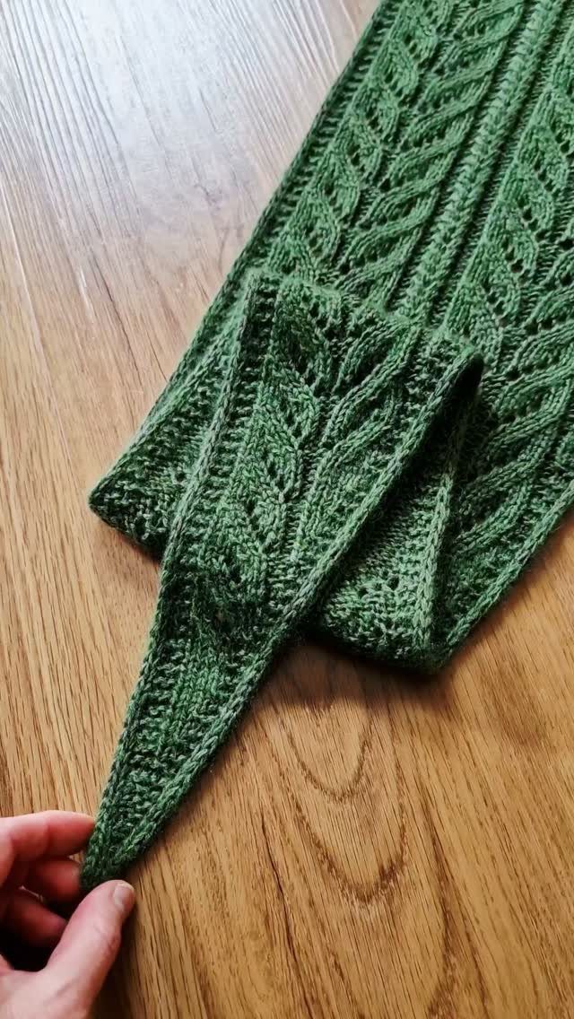 Green knitted scarf with cable patterns resting on a light wooden table.