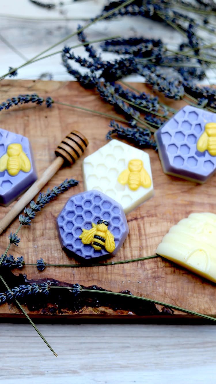Hexagonal purple and white soaps with yellow bees on a wooden board with lavender.