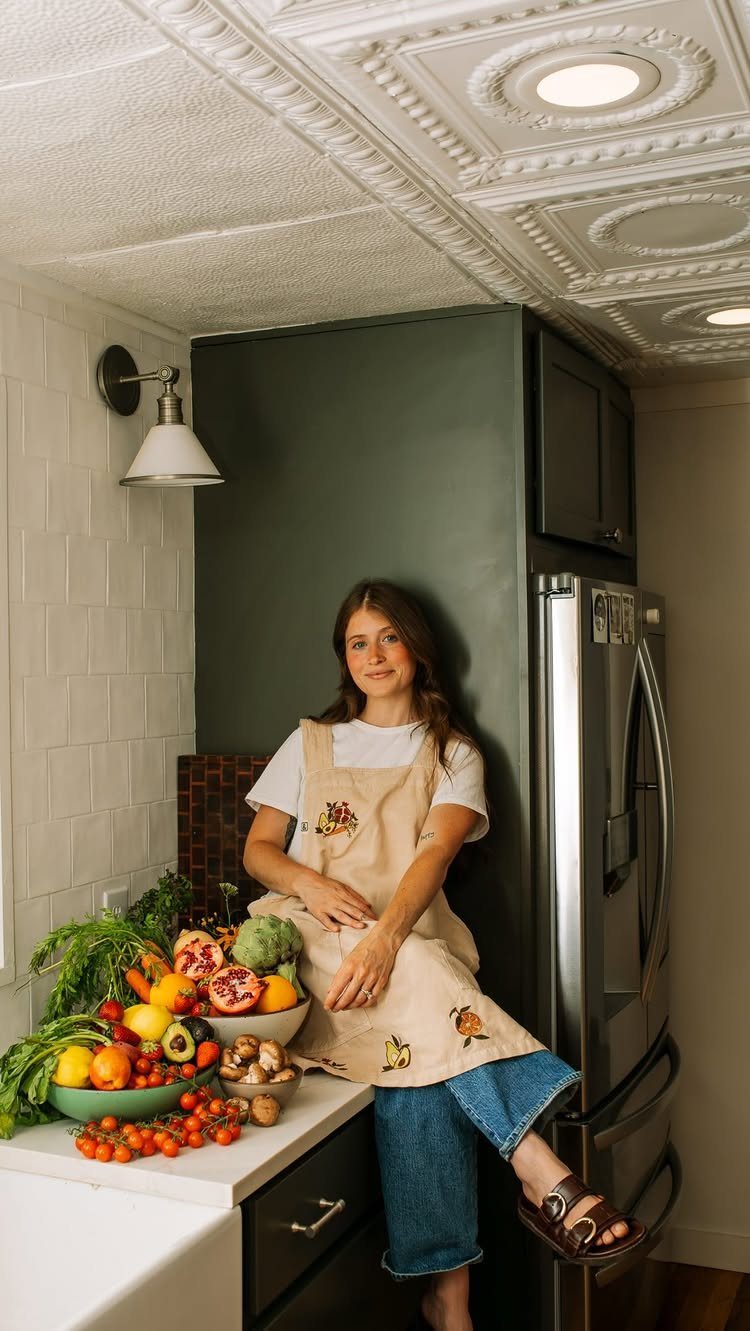 Woman wearing a beige linen apron with fruit embroidery in a modern kitchen.