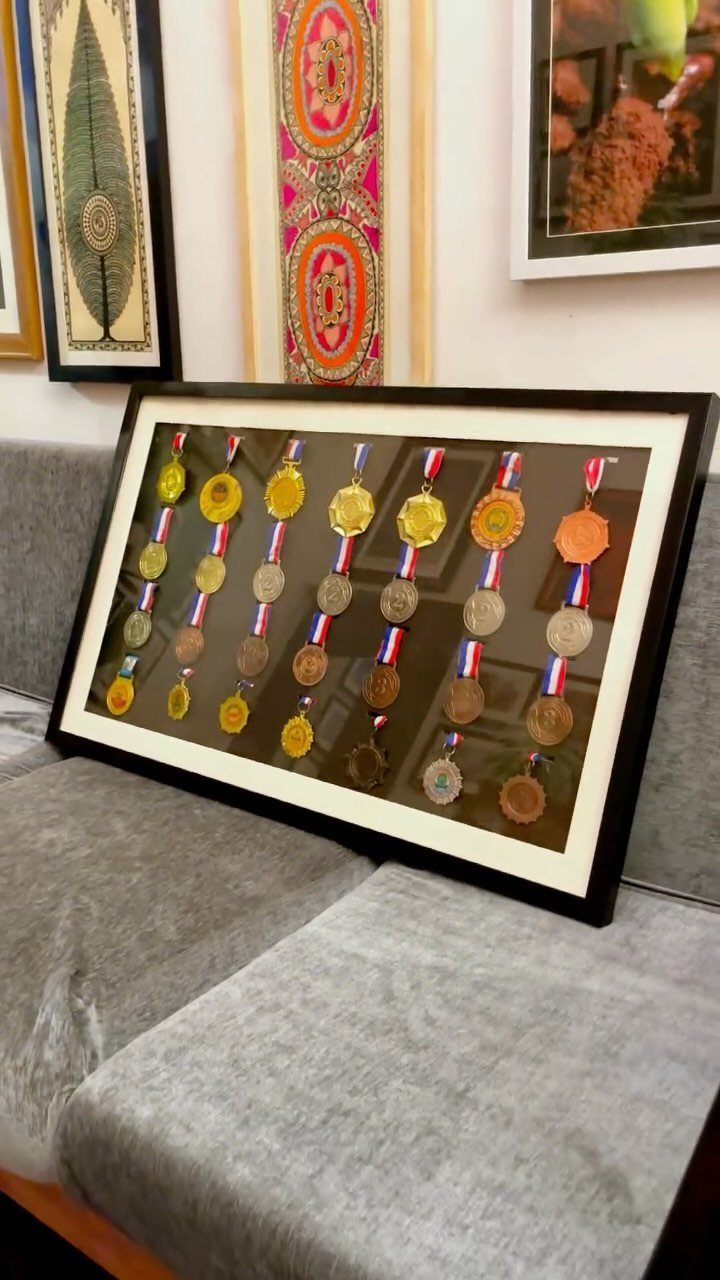 Black framed shadow box displaying multiple gold and bronze medals on colorful ribbons.