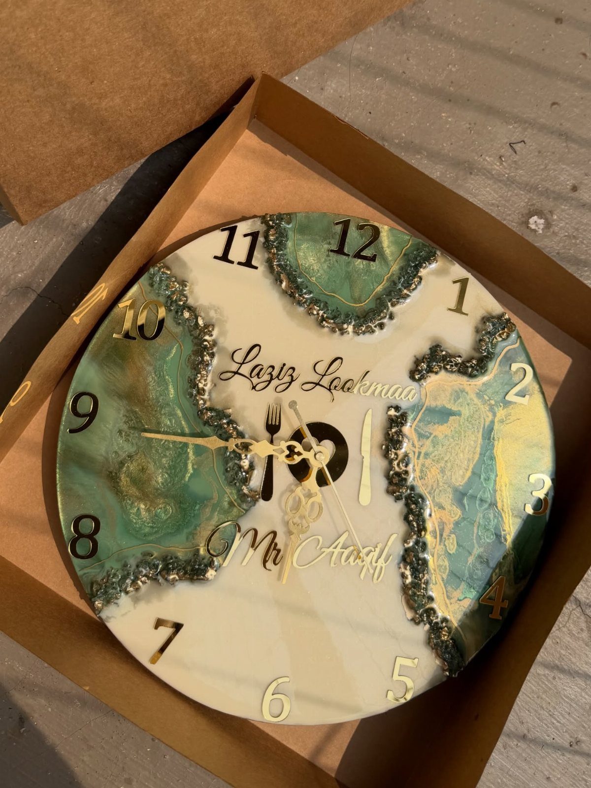 Resin art clock with green and gold marbled patterns in a cardboard box