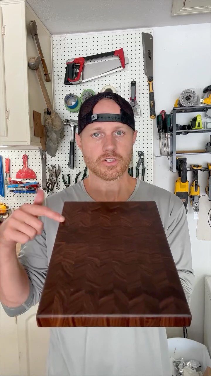 Man holding a polished dark brown wooden cutting board in a tool workshop.