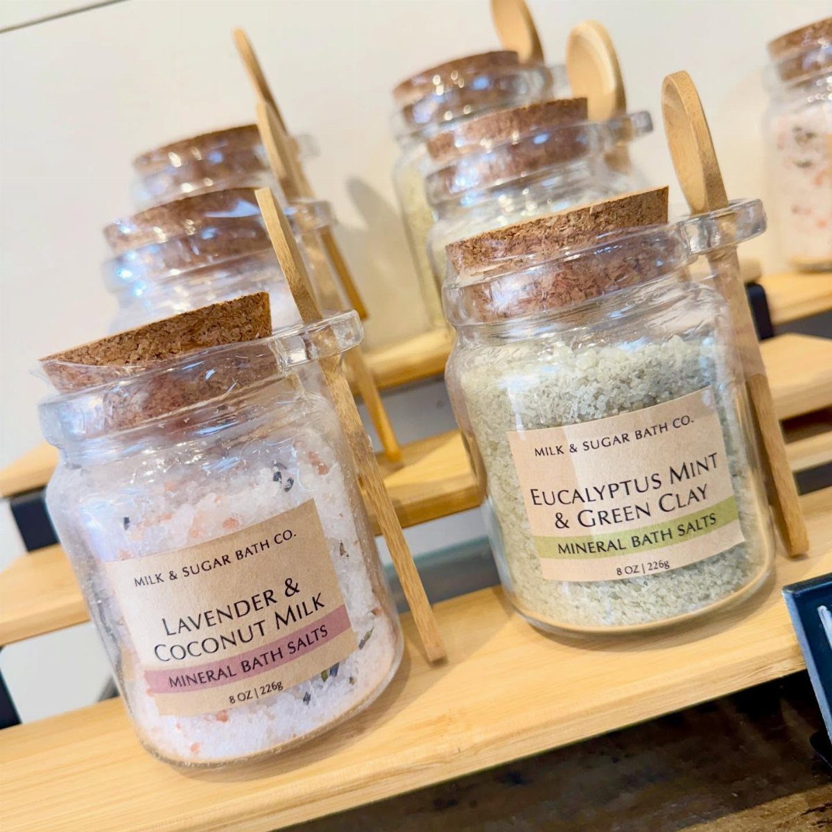 Glass jars filled with colorful mineral bath salts on wooden display shelves.
