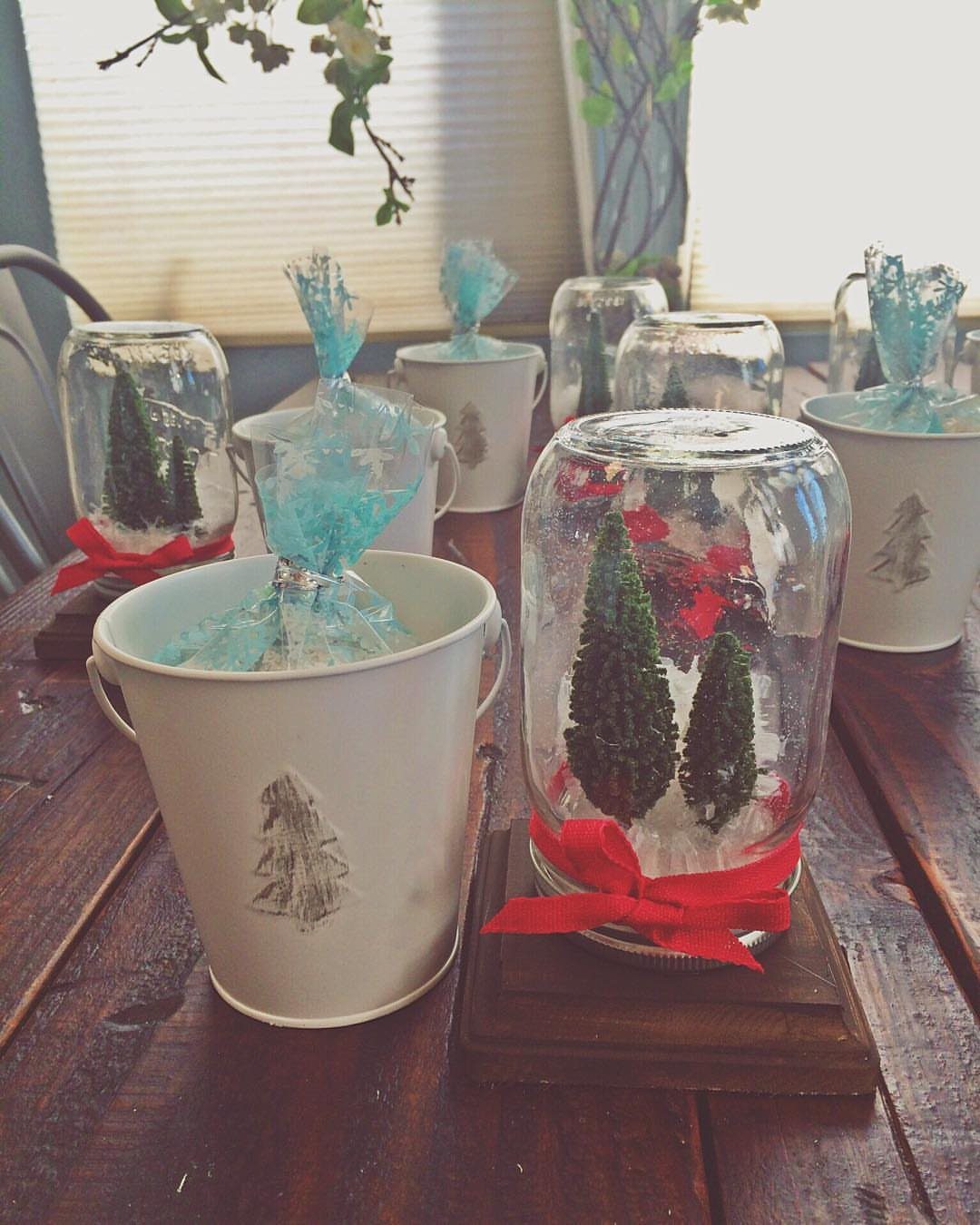 Mason jars with miniature evergreen trees and red ribbons on a wooden table.