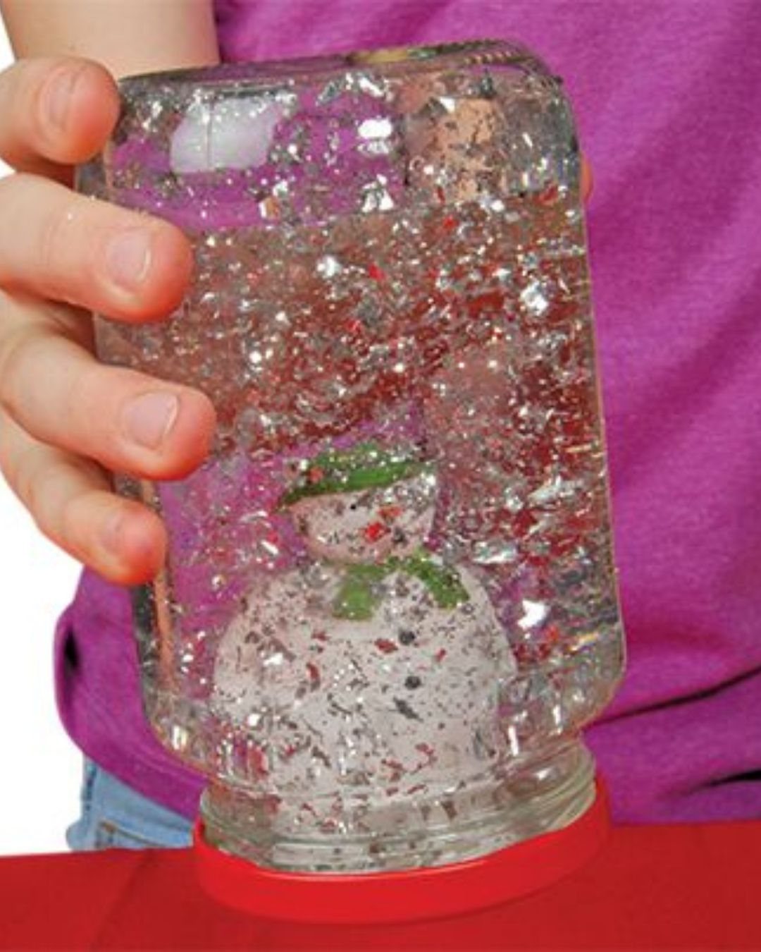 Mason jar snow globe with a small snowman and silver glitter inside.