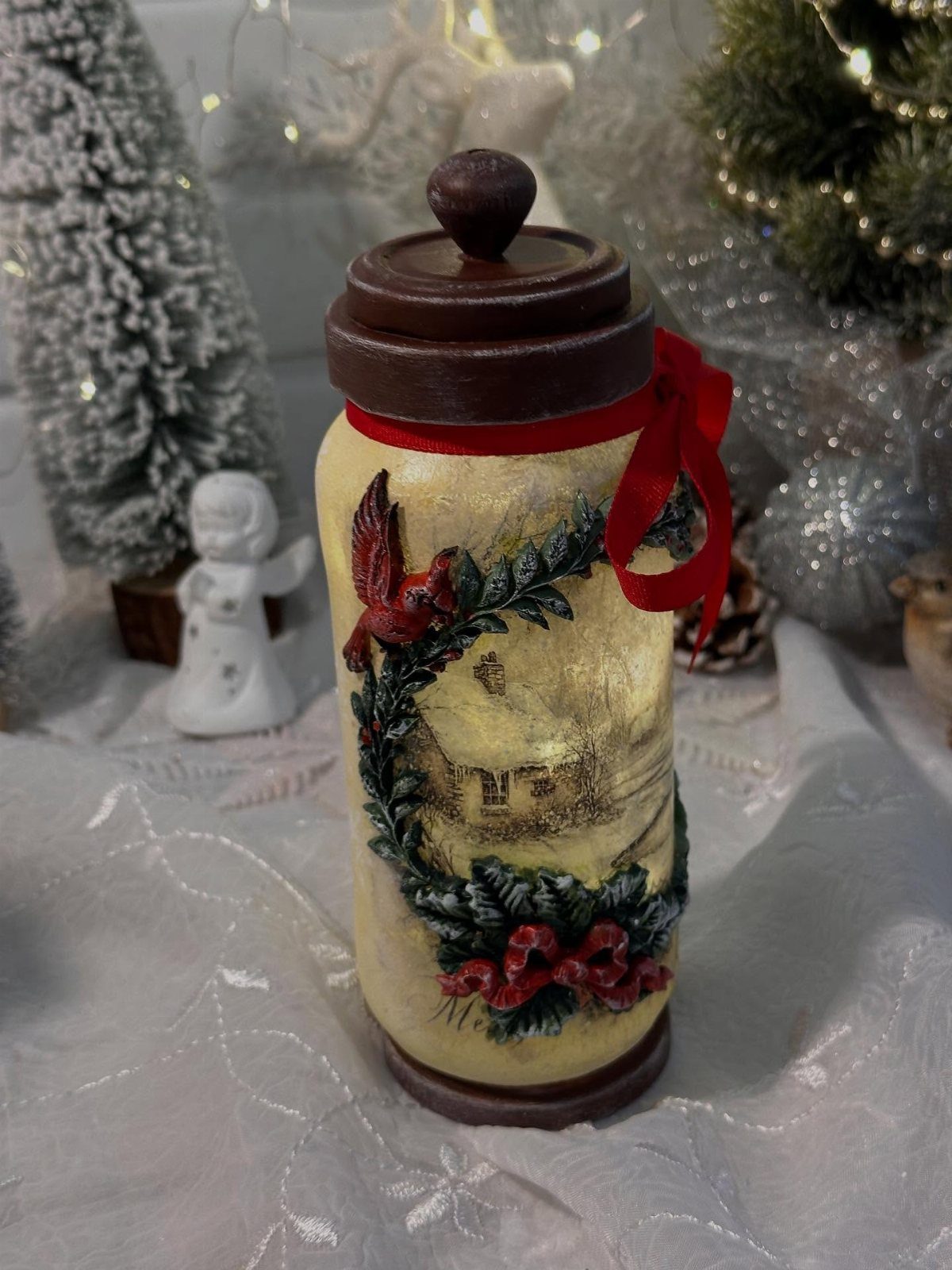 Decorated mason jar with winter scene relief, red ribbon, and brown lid.