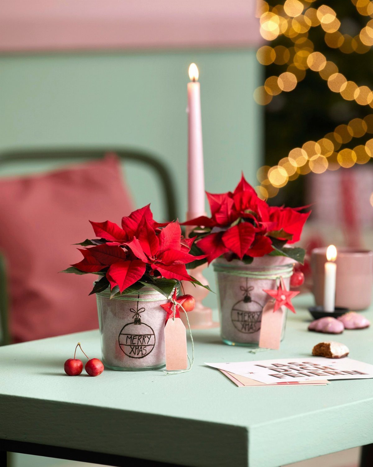 Glass jars with red poinsettia flowers and Merry Xmas labels on a table.